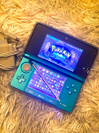 Nintendo 3DS gaming console with a blue shell displaying the 'Pokémon' game on a textured surface.