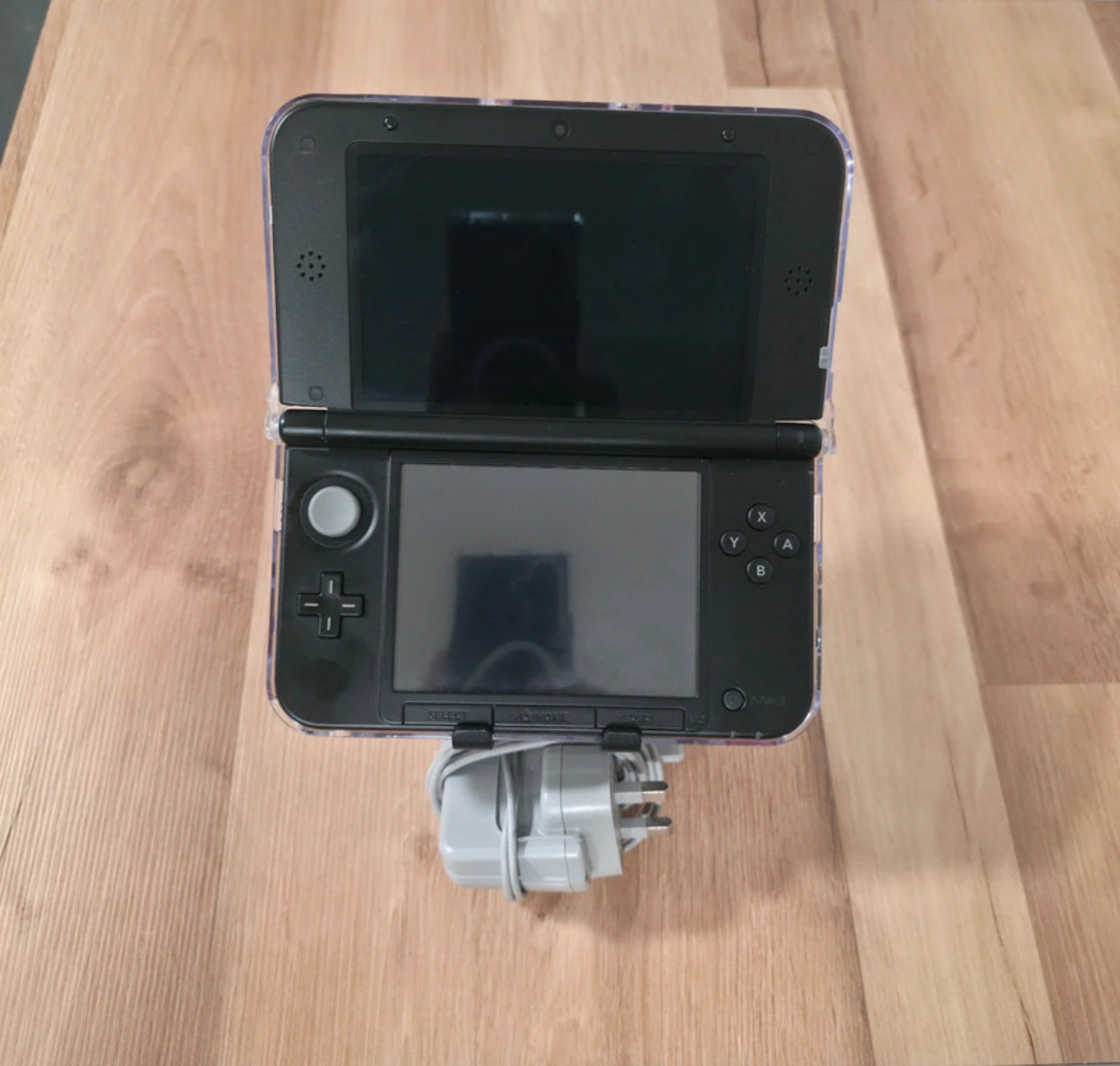 Black handheld gaming console with a strap on a wooden surface Modified Nintendo 3DS XL with custom firmware, Luma3DS, homebrew apps, emulators, customizable themes, and enhanced performance features.