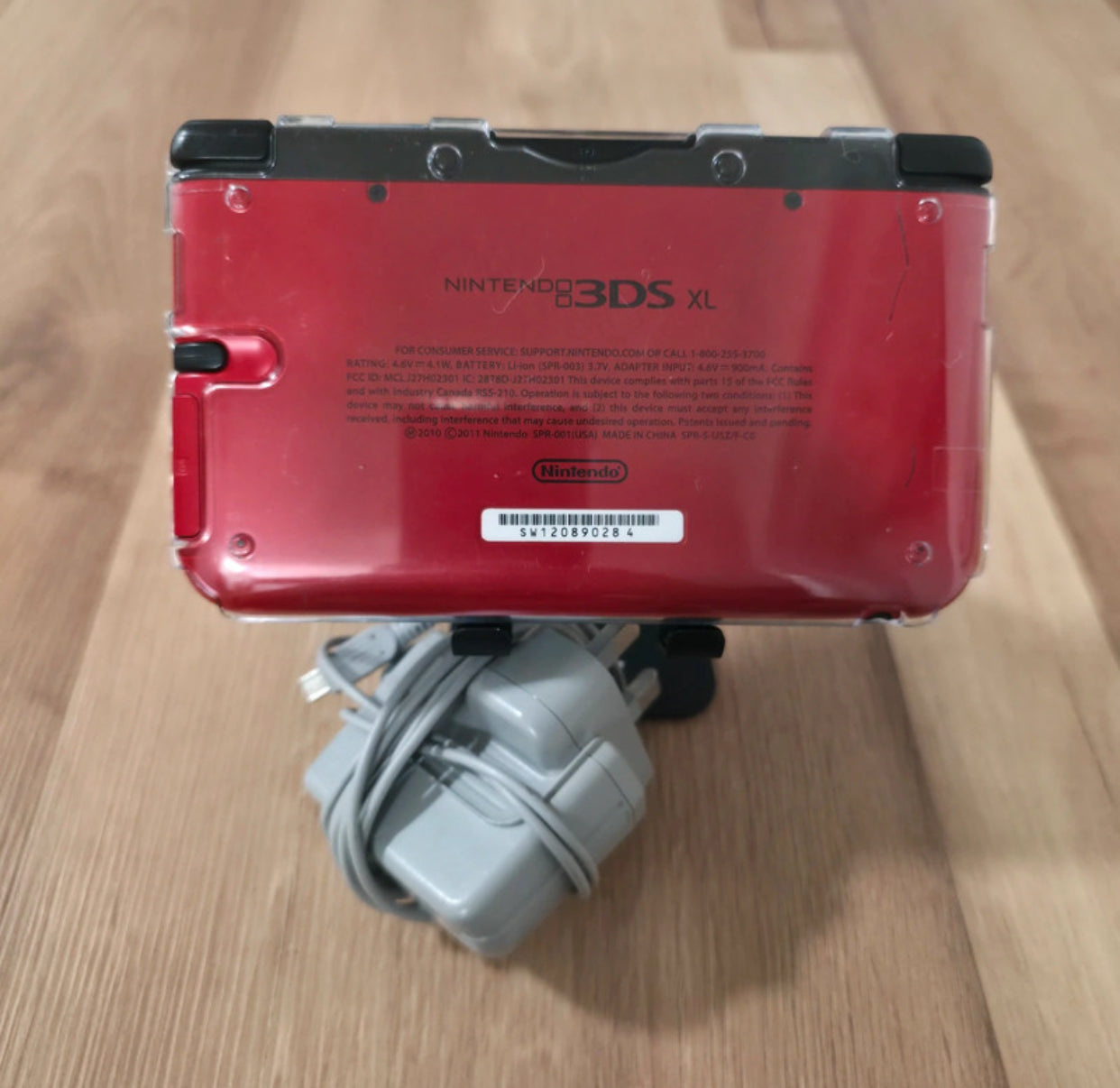 Red Nintendo 3DS XL gaming console with charger on a wooden surface Modified Nintendo 3DS XL with custom firmware, Luma3DS, homebrew apps, emulators, customizable themes, and enhanced performance features.