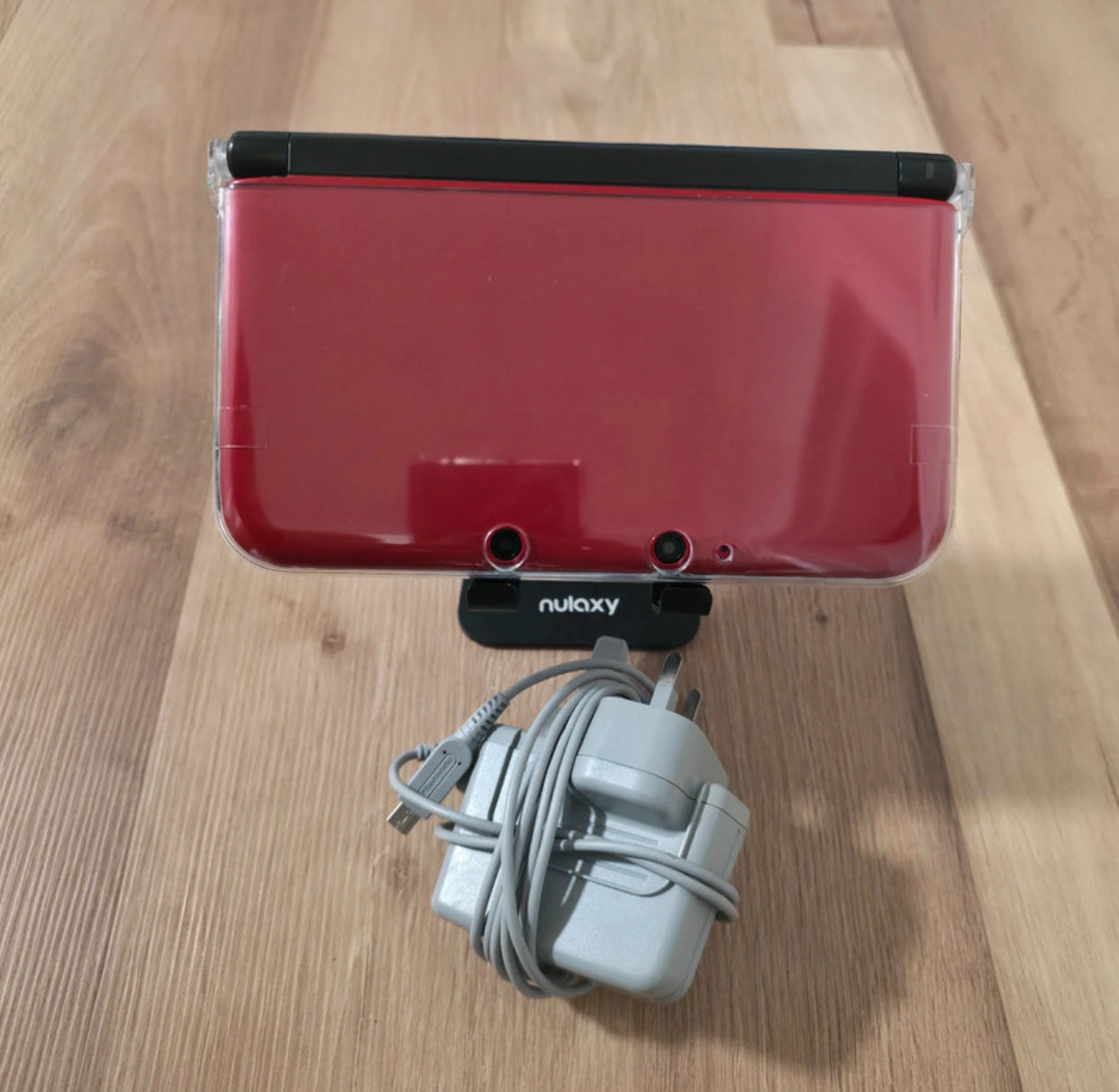 Red electronic device with a cable on a wooden surface Modified Nintendo 3DS XL with custom firmware, Luma3DS, homebrew apps, emulators, customizable themes, and enhanced performance features.