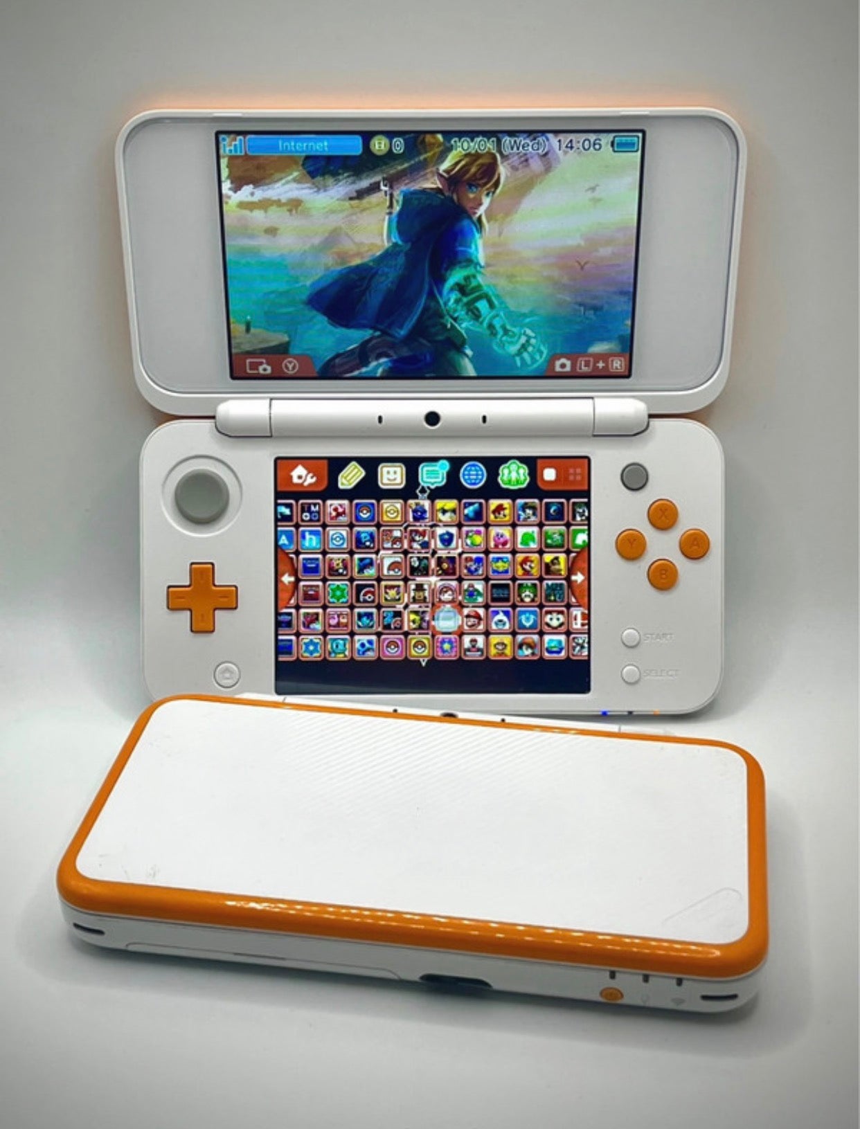 Handheld gaming console with open lid showing game selection screen and closed lid. Custom modded Nintendo 2DS XL white orange with 128GB SD card pre-installed games emulators homebrew CFW UK professional modding service
