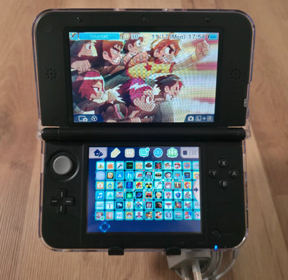 Nintendo 3DS gaming console displaying a colorful game interface on a wooden surface Modified Nintendo 3DS XL with custom firmware, Luma3DS, homebrew apps, emulators, customizable themes, and enhanced performance features.