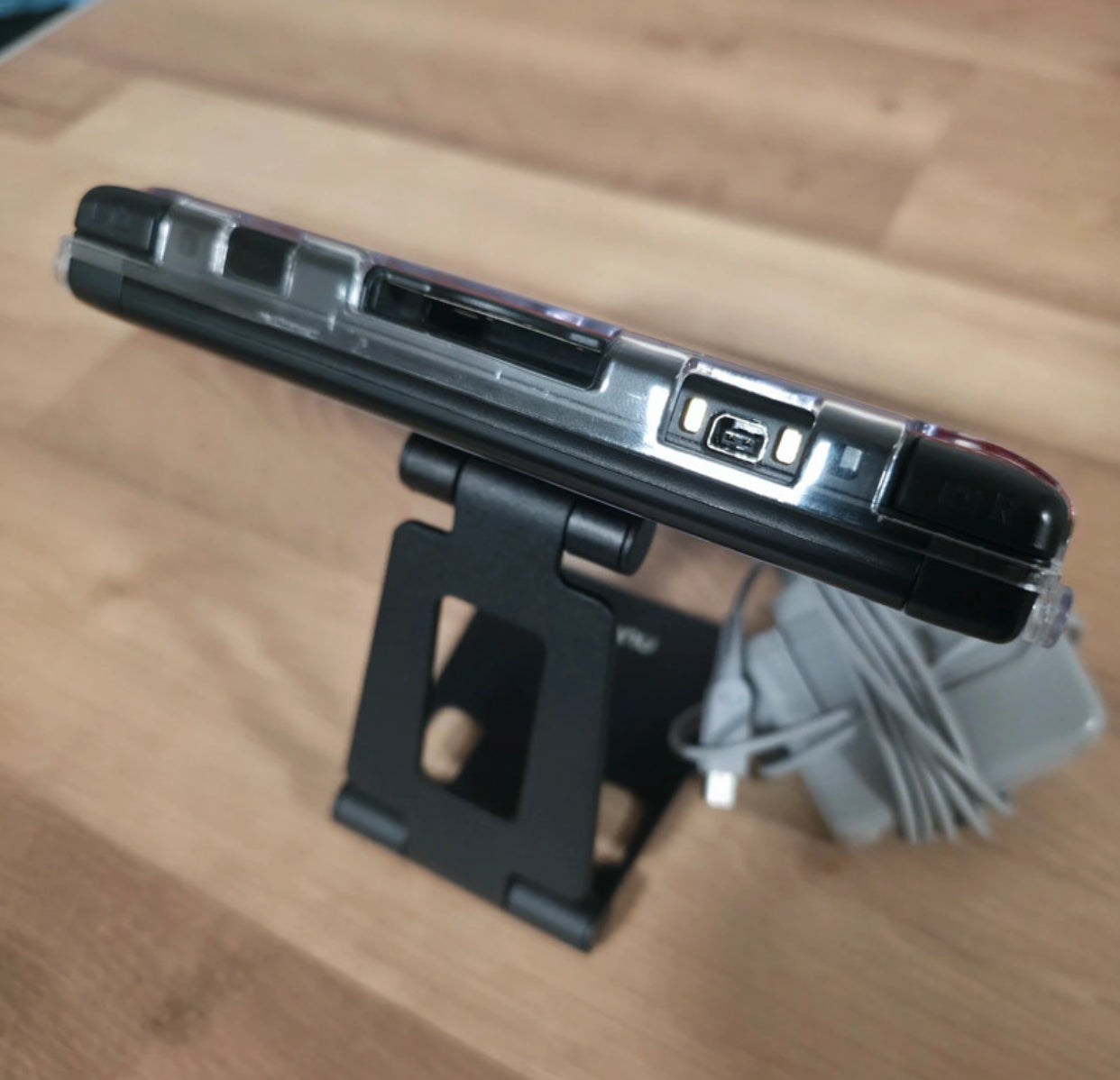 3DS stand and cable on a wooden surface Modified Nintendo 3DS XL with custom firmware, Luma3DS, homebrew apps, emulators, customizable themes, and enhanced performance features.