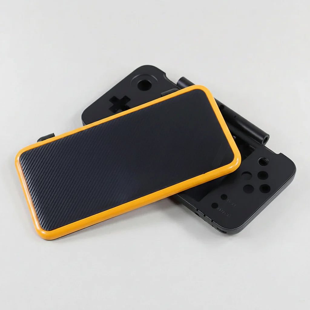 Two assembled Ghost Signal New 2DS XL shells in black carbon with orange trim, stacked at an angle
