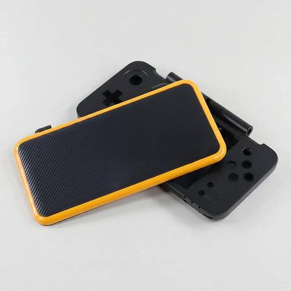 Two assembled Ghost Signal New 2DS XL shells in black carbon with orange trim, stacked at an angle