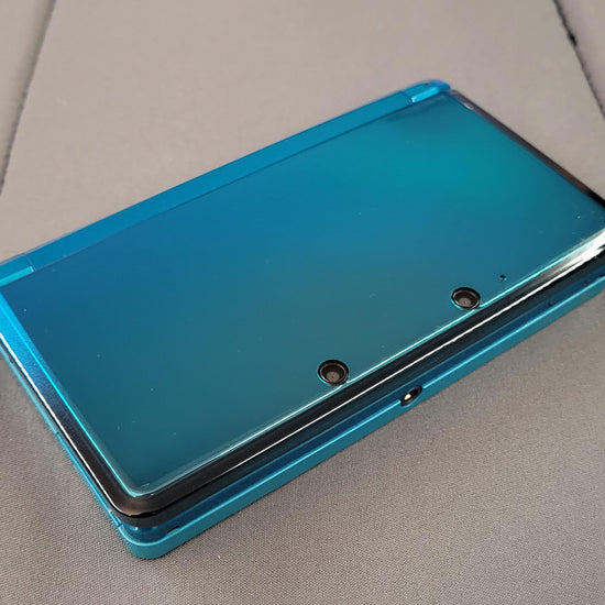 Video showing a modded Nintendo 3DS with 128GB storage running custom firmware, featuring a custom theme interface, Homebrew menu, and various installed emulator apps. Clear plastic case with branding on a blue and wooden surfacePink handheld gaming device with screen displaying 'Super Smash Bros.' game on a glittery gold surface. 3DS Modded 3DS Custom Firmware 128gb emulators, anemone, h shop, homebrew