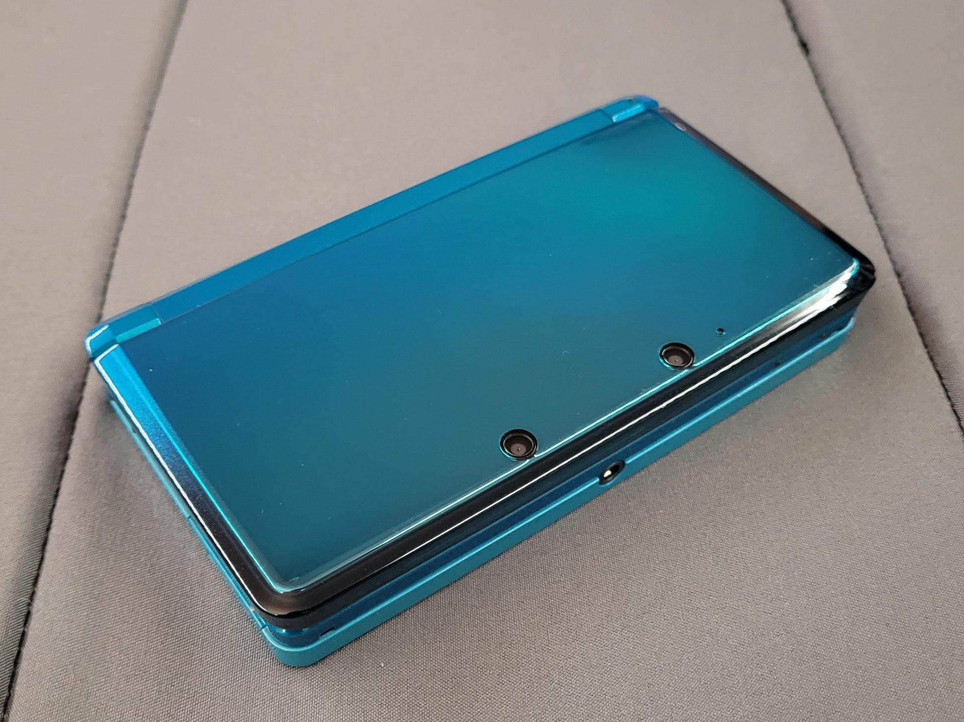 Video showing a modded Nintendo 3DS with 128GB storage running custom firmware, featuring a custom theme interface, Homebrew menu, and various installed emulator apps. Clear plastic case with branding on a blue and wooden surfacePink handheld gaming device with screen displaying 'Super Smash Bros.' game on a glittery gold surface. 3DS Modded 3DS Custom Firmware 128gb emulators, anemone, h shop, homebrew