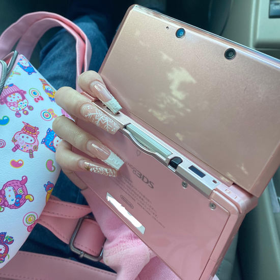 Video showing a modded Nintendo 3DS with 128GB storage running custom firmware, featuring a custom theme interface, Homebrew menu, and various installed emulator apps. Clear plastic case with branding on a blue and wooden surfacePink handheld gaming device with screen displaying 'Super Smash Bros.' game on a glittery gold surface. 3DS Modded 3DS Custom Firmware 128gb emulators, anemone, h shop, homebrew