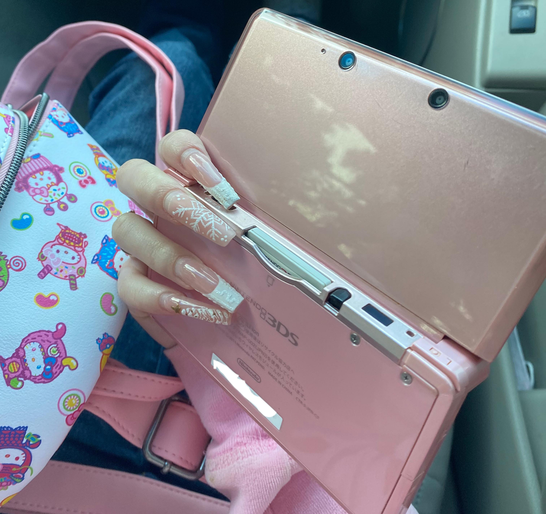 Video showing a modded Nintendo 3DS with 128GB storage running custom firmware, featuring a custom theme interface, Homebrew menu, and various installed emulator apps. Clear plastic case with branding on a blue and wooden surfacePink handheld gaming device with screen displaying 'Super Smash Bros.' game on a glittery gold surface. 3DS Modded 3DS Custom Firmware 128gb emulators, anemone, h shop, homebrew